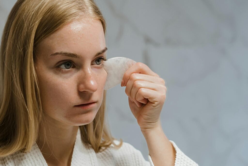 Close-up of a woman performing a facial massage with a gua sha tool for skincare and self-care.