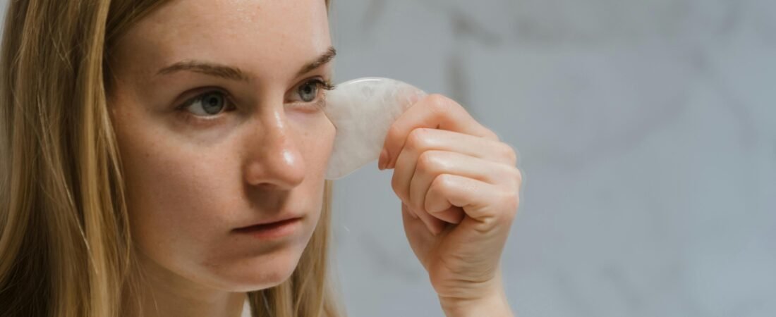 Close-up of a woman performing a facial massage with a gua sha tool for skincare and self-care.